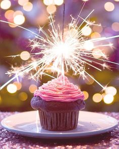 a cupcake with pink frosting and sparklers on it sitting on a plate