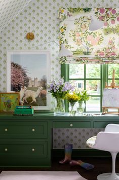 a green desk with flowers and pictures on the wall next to it in front of a window