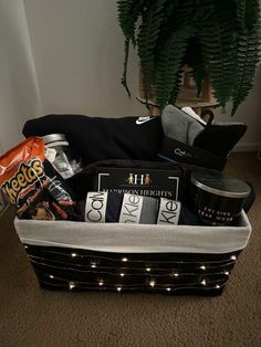 a basket filled with snacks and drinks on top of a carpeted floor next to a potted plant