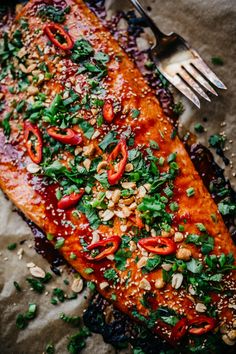 a piece of salmon covered in red sauce and garnished with green onions, cilantro, and peanuts