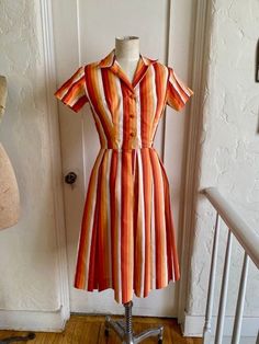 This is a great 50s shirt waist dress by Meo of California. Shades of orange and ivory stripes with button front with hook and eye at waist. Pleated skirt 100% Dacron. Size label says 9 but that's a vintage size so I would say 4/6 contemporary. Measurements flat are 17" underarm to underarm 12 1/2" waist. Retro Orange Lined Dress, Fitted Retro Dresses With Vertical Stripes, Orange Retro Dress With Retro Print, Vintage Orange Dress For Daywear, Orange Vintage A-line Dress, Vintage Pleated Cotton Dress, Retro Fitted Dress With Vertical Stripes, Striped Retro Dresses With Buttons, Retro A-line Dress With Box Pleat