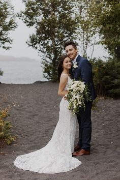 a bride and groom pose for a photo on the beach