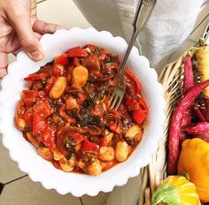 a person is holding a bowl of food with a fork in it and some vegetables on the side