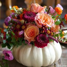 a white pumpkin filled with lots of flowers on top of a wooden table next to a plate