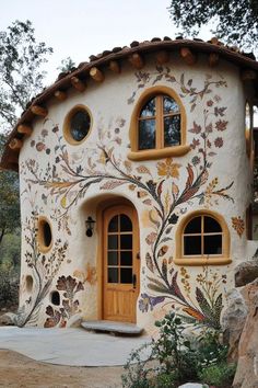 a small house made out of stucco with windows and flowers painted on the outside wall