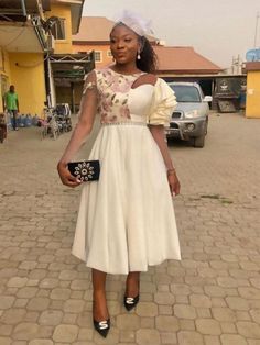 a woman in a white dress standing on a cobblestone street with a black purse