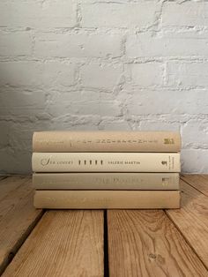 three books stacked on top of each other in front of a white brick wall and wooden floor