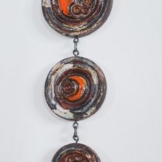 two circular metal objects hanging from chains on a white wall with orange circles in the center