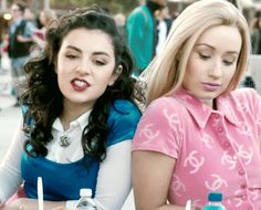 two young women sitting at a table with drinks in front of them and one is holding a cell phone