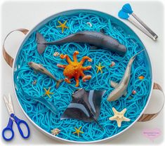 a bowl filled with blue noodles and sea animals on top of it next to scissors