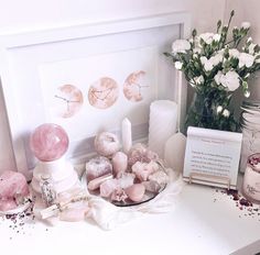 a white table topped with lots of pink and white items next to a vase filled with flowers