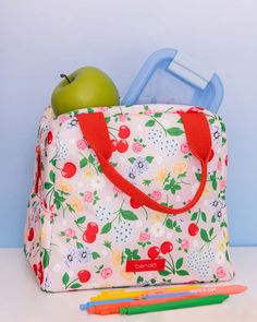 a lunch bag with an apple and some colored pencils next to it on a table