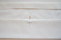 a piece of white fabric with pins sticking out of the top and bottom of it