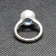 a silver ring sitting on top of a gray surface with a blue stone in the middle