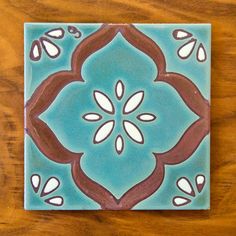 a blue tile with brown and white designs on the bottom is sitting on a wooden table