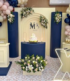 a table topped with a cake surrounded by balloons and flowers in front of a stage