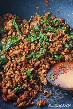 a pan filled with meat and spinach on top of a wooden spoon in it