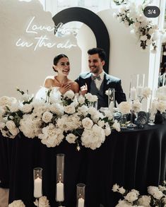 a man and woman standing next to each other in front of a table with flowers