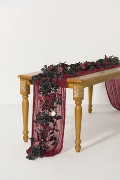 a wooden table topped with a red and black floral covered runner on top of it