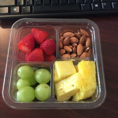 a plastic container filled with fruit and nuts next to a computer keyboard on a desk