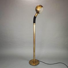 a gold and black floor lamp with a white light on the top, in front of a gray background