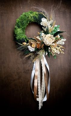 a wreath with white flowers and greenery hanging on a wooden wall next to a ribbon