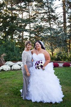 two women standing next to each other in front of trees and flowers on the grass