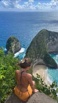 a woman sitting on top of a cliff overlooking the ocean