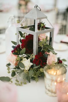 a small lantern with flowers and greenery on the table at a wedding reception or party