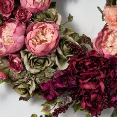 a bunch of flowers that are sitting on a white surface with green leaves and berries