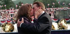 a man and woman kissing each other in front of an outdoor stage full of people