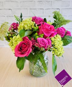 a glass vase filled with pink roses and green leaves on top of a wooden table