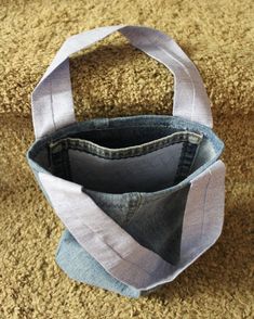 an empty bag sitting on the floor next to a pair of jeans and a purse