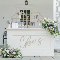 an outdoor bar with flowers and greenery on the counter at a wedding reception in front of a white building