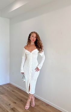 a woman standing in a room wearing a white sweater dress with thigh high slits