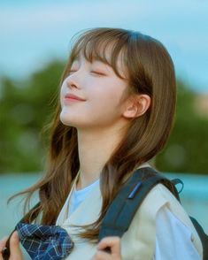 a young woman with her eyes closed wearing a backpack and looking up at the sky