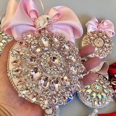 a hand holding several pairs of shoes with pink bows on them, and one shoe has been decorated with swarozak crystals