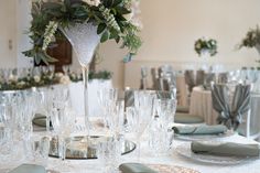 the table is set with silverware and white flowers in a tall glass vase on top