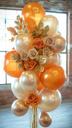 an arrangement of orange and white balloons in a vase with flowers on the top, against a brick wall