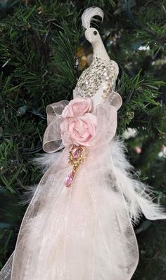 a white bird ornament hanging from a christmas tree with pink flowers and feathers