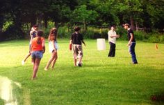 a group of people playing frisbee in the grass with trees in the background