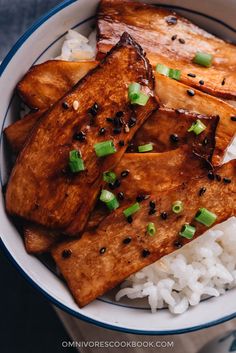 a white bowl filled with rice and tofu topped with scallions on top