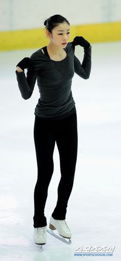 a woman skating on an ice rink wearing black pants and a gray shirt with her hands behind her head