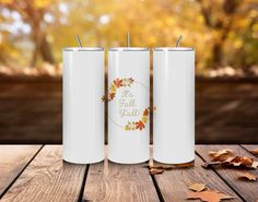 three white tumbles sitting on top of a wooden table next to leaves and autumn leaves