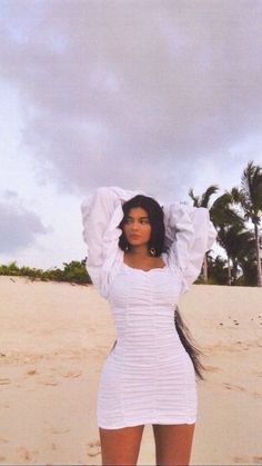 a woman standing on top of a beach next to the ocean wearing a white dress