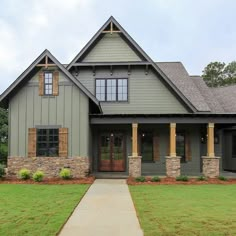 a gray house with brown shutters on the front and side windows, grass in front