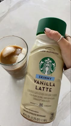 a hand holding a bottle of starbucks vanilla latte next to a cup of coffee