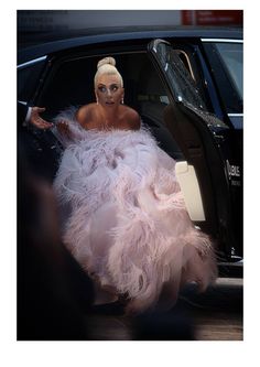 a woman in a pink feathered dress stepping out of a black car with the door open