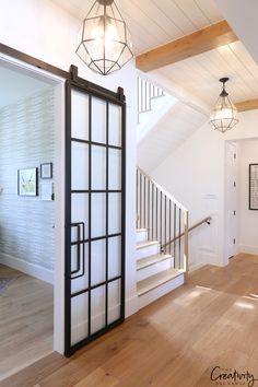 an open door leading to a hallway with wooden floors and white walls, along with two chandeliers hanging from the ceiling