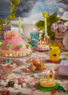 a table topped with cakes and candles on top of a table covered in food items